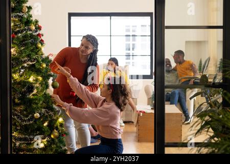 Famille multiraciale décorant l'arbre de Noël ensemble, partageant des moments joyeux à la maison Banque D'Images