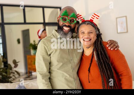 Heureux couple multiracial portant des accessoires de fête, souriant ensemble à la maison pendant Noël Banque D'Images