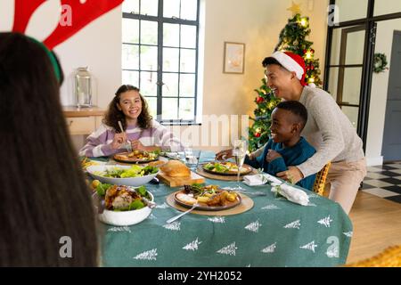 Famille multiraciale profitant d'un repas de Noël festif ensemble, souriant autour de la table décorée, à la maison Banque D'Images