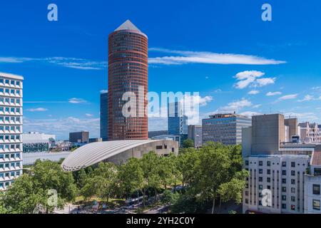 Un gratte-ciel saisissant présente une architecture contemporaine, entouré de verdure luxuriante et d'autres bâtiments, assis contre un ciel bleu clair pendant la journée Banque D'Images