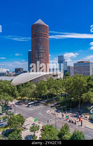 Un gratte-ciel saisissant présente une architecture contemporaine, entouré de verdure luxuriante et d'autres bâtiments, assis contre un ciel bleu clair pendant la journée Banque D'Images