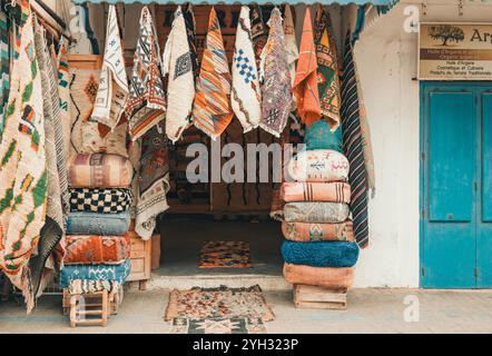 Tapis berbères marocains à motif traditionnel, tapis et textiles accrochés dans un étal de marché animé, souks dans la vieille ville Medina, Essaouira, Maroc Banque D'Images