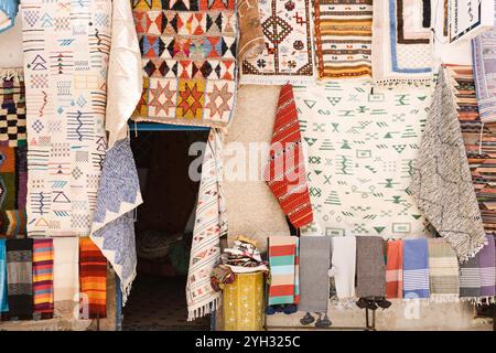 Tapis berbères marocains à motif traditionnel, tapis et textiles accrochés dans un étal de marché animé, souks dans la vieille ville Medina, Essaouira, Maroc Banque D'Images