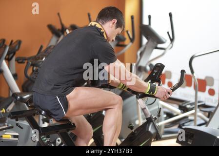 Homme musclé faisant du vélo dans le gymnase, exerçant des jambes faisant du vélo d'entraînement cardio vélo, cours de spinning Banque D'Images