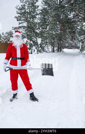 Le Père Noël nettoie la neige avec une pelle en hiver à l'extérieur après une chute de neige. Nettoyer les rues du village, dégager le passage pour les voitures, difficile Banque D'Images