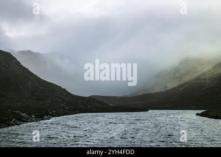 Une rivière sereine serpente à travers une zone montagneuse, enveloppée de brume. Le brouillard enveloppe doucement les collines, créant une atmosphère calme et paisible dans le th Banque D'Images