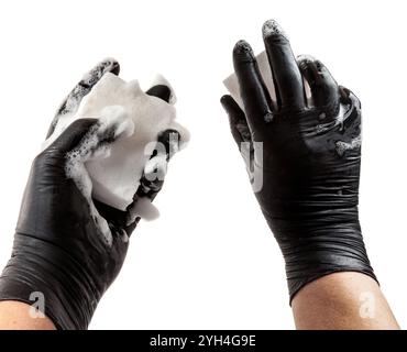 Mains dans un gant de protection en caoutchouc noir. Mains tient une éponge dans la mousse. Le processus de lavage de la vaisselle ou de nettoyage. Isolé sur blanc Banque D'Images