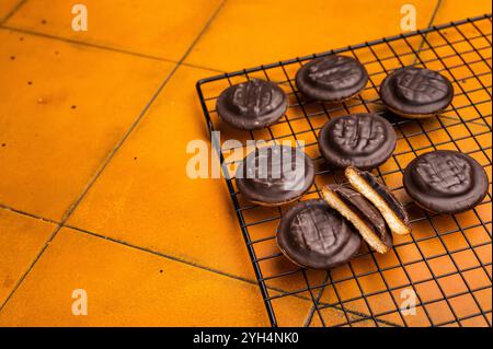 Biscuits Jaffa fraîchement cuits recouverts de chocolat et remplis de confiture sur grille. fond orange. vue de dessus. Banque D'Images