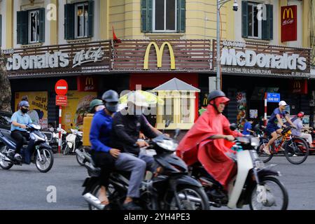 Hanoi, Vietnam - 5 juillet 2023 : les gens passent leur moto devant un restaurant de restauration rapide McDonald's dans une rue animée du centre-ville de Hanoi. Banque D'Images