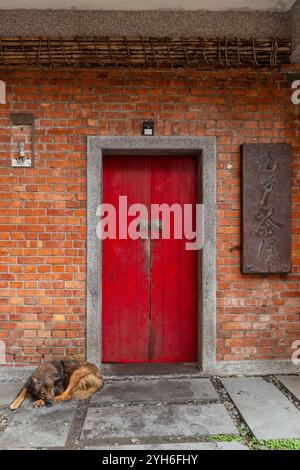 Un chien dort devant une porte rouge rustique et un mur de briques dans le village de Juifen, Taiwan Banque D'Images