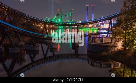 Une photo de nuit captivante d'Universal Orlando avec des montagnes russes aux lumières vibrantes reflétées dans l'eau, créant une atmosphère animée. Banque D'Images