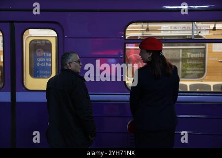 Bakou, Azerbaïdjan, Azerbaïdjan. 10 novembre 2024. Un guide de métro en uniforme et chapeau rouge parle au cavalier devant une voiture de métro violette. (Crédit image : © Bianca Otero/ZUMA Press Wire) USAGE ÉDITORIAL SEULEMENT! Non destiné à UN USAGE commercial ! Banque D'Images