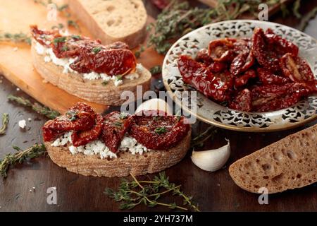 Sandwich ouvert avec tomates séchées maison et fromage cottage. Tomates séchées au soleil dans l'huile d'olive avec thym et ail sur une vieille table en bois. Banque D'Images