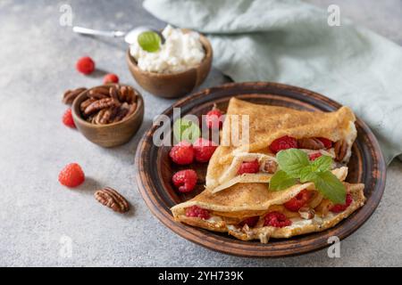 Savoureuses crêpes sucrées maison farcies aux framboises et au fromage à la crème sur un fond de pierre grise. Crêpes fines, blini. Dessert sucré. Banque D'Images