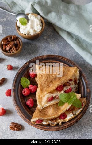Savoureuses crêpes sucrées maison farcies aux framboises et au fromage à la crème sur un fond de pierre grise. Crêpes fines, blini. Dessert sucré. Banque D'Images