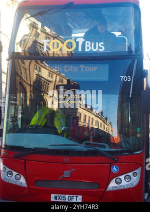 Bus touristique Toot rouge à toit ouvert avec une partie de l'architecture géorgienne en pierre de Bath, y compris une partie de l'abbaye de Bath reflétée dans le pare-brise Banque D'Images