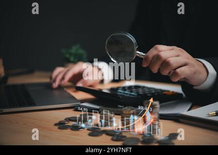 Main tenant une loupe sur des pièces avec des graphiques de tendance à la hausse. Banque D'Images