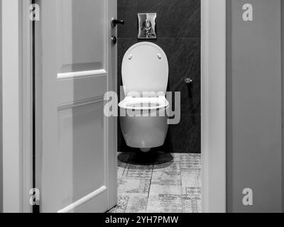 Cuvette de toilette en céramique blanche de luxe propre à l'intérieur de la salle de toilette avec porte upvc sur le mur de granit noir et sol en marbre, vue avant dans la salle de bain moderne int Banque D'Images