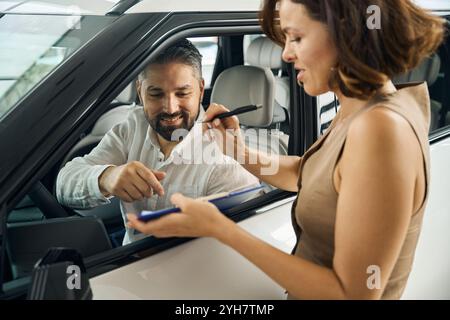 Client masculin qui signe des documents, vendeur féminin qui tient des documents Banque D'Images