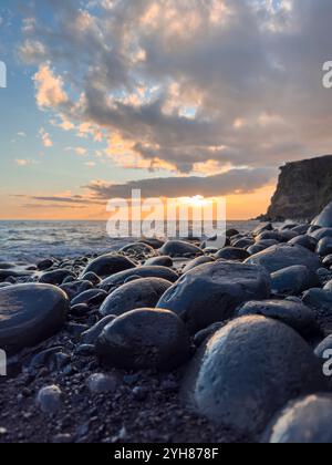 Coucher de soleil sur un rivage rocheux de l'océan avec le ciel spectaculaire et l'éclat du soleil sur les rochers humides. Vertical. Madère, Portugal. Banque D'Images