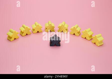 Figures en bois d'un groupe de jaune et une forme humaine noire sur un fond rose.. Banque D'Images