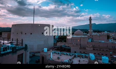 Vue panoramique sur le coucher du soleil du Fort de Nizwa avec la ville et la mosquée Al Qalaa à Nizwa, Oman Banque D'Images
