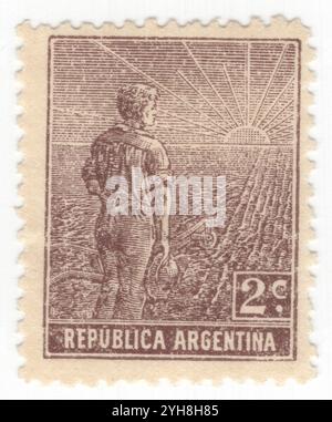 ARGENTINE - 1911 : 2 centavos timbre-poste en chocolat représentant un ouvrier agricole, composition allégorique Agriculture. Un jeune agriculteur avec une charrue au bord d'un champ partiellement labouré regarde le lever du soleil. Un symbole de la réforme agricole et de la formation de l'Argentine comme puissance mondiale dans la production agricole Banque D'Images