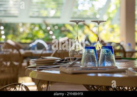 Verres et couverts sur une table de restaurant dans un cadre tropical ensoleillé avec stores en arrière-plan Banque D'Images