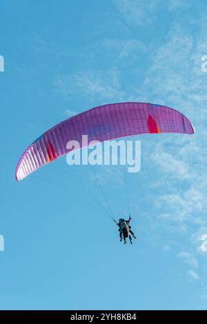 Les parapentes en tandem s'élèvent au-dessus du paysage sous une canopée rose vibrante par une journée ensoleillée claire Banque D'Images