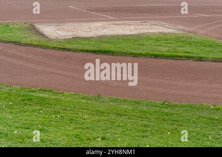 Sablier de saut long et piste de course avec de l'herbe verte sur une journée nuageuse Banque D'Images