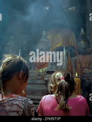 Laos, Champasak, Wat Phu : le festival annuel Wat Phu Champasak attire des gens et des moines de tout le Laos. Deux filles prient devant des divinités de pierre. Banque D'Images