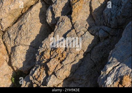 La lumière du soleil projette de belles ombres sur les rochers côtiers texturés, révélant de superbes formations naturelles au crépuscule. Banque D'Images