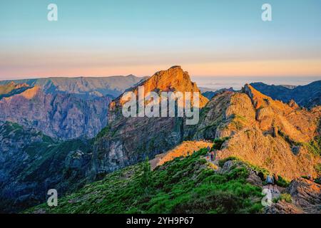 Une vue au lever du soleil depuis un sommet de montagne avec des randonneurs sur un sentier pittoresque, entouré par un terrain rocheux accidenté. Banque D'Images