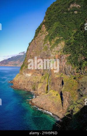 Une superbe image de paysage montrant une falaise accidentée en cascade dans l'océan. La lumière du soleil illumine la verdure luxuriante et le terrain rocheux. Banque D'Images