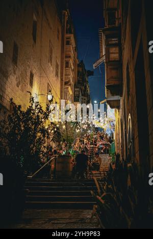 Une scène de soirée animée dans une rue étroite avec salle à manger en plein air et guirlande de lumières d'ambiance. Les gens apprécient leur temps dans les escaliers. Banque D'Images