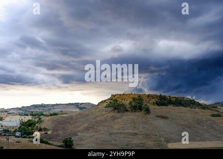 Une vue d'une colline avec des arbres dispersés, encadrée par des nuages spectaculaires et orageux sur un paysage rural au coucher du soleil. Banque D'Images