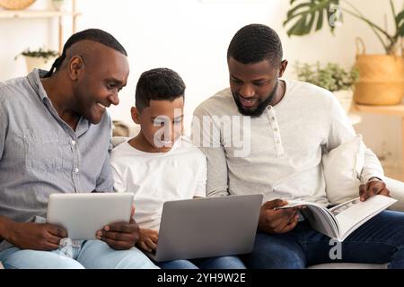 Famille africaine avec ordinateur portable, tablette numérique et magazine à la maison Banque D'Images