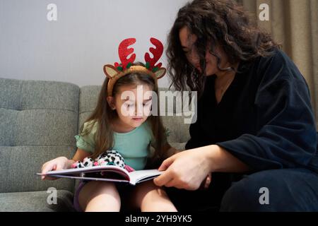 Mère et fille partagent la joie des vacances tout en lisant un livre sur le canapé Banque D'Images