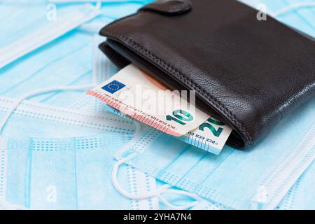 Portefeuille noir pour homme avec de l'argent en euros à l'intérieur sur les masques médicaux jetables bleus. Échange de masques médicaux. Affaires pendant une pandémie ou une épidémie Banque D'Images