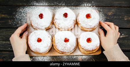 Cuisine traditionnelle Hanukkah sufganiyot. Femme saupoudre les beignets de sucre en poudre. Tient la main Berliner avec de la confiture. Format de bannière. Banque D'Images