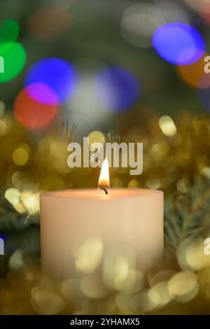 Bougie blanche de Noël brûlant tranquillement, avec des reflets bokeh colorés autour d'elle Banque D'Images