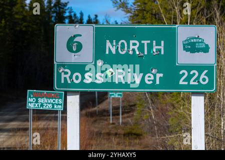 Panneau routier de Ross River dans le nord du Canada, territoire du Yukon vu pendant l'été avec des trous de balles dans les panneaux routiers. Banque D'Images