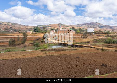 Une scène rurale tranquille à Madagascar, avec des champs en terrasses vertes et brunes. Un village lointain peut être vu niché parmi les collines ondoyantes. L'image Banque D'Images