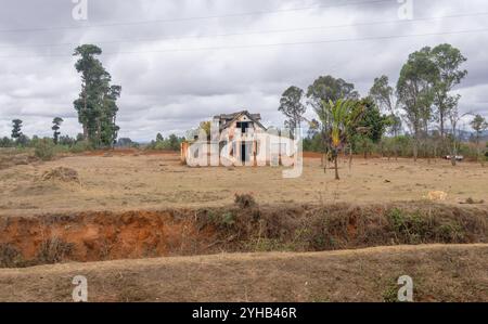 Une maison abandonnée en briques rouges se tient seule au milieu d'un champ. La route menant au parc est bordée de ce paysage rustique. Isalo National par Banque D'Images