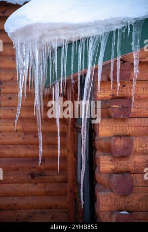 Pendants longs glaçons vus sur le côté d'une magnifique cabane en rondins, maison, construction de maison avec des bords tranchants en saison d'hiver. Banque D'Images