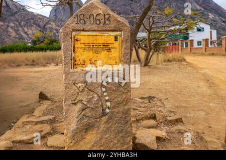 Parc national d'Isalo, Madagascar - 30 août 2024 : marqueur en pierre historique avec motif de lémuriens sculptés. Montagnes de granit et végétation indigène visibles dans Banque D'Images