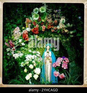 Plastic flowers surround a sculpture of the Virgin Mary in Benamahoma, Sierra de Grazalema Natural Park, Cadiz province, Andalusia, Spain. Stock Photo