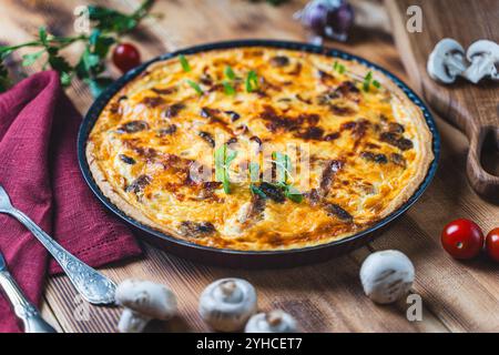 Quiche ou tarte avec de la viande, du poulet et des champignons sur une table en bois avec couverts, herbes et tomates cerises. Photo de haute qualité Banque D'Images