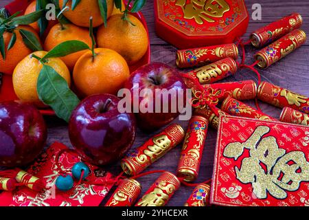 Gros plan d'une assiette de mandarines et de pommes rouges. Décorations lunaires du nouvel an et paquets rouges avec bonne fortune, santé, mots de richesse sur eux. A Chines Banque D'Images