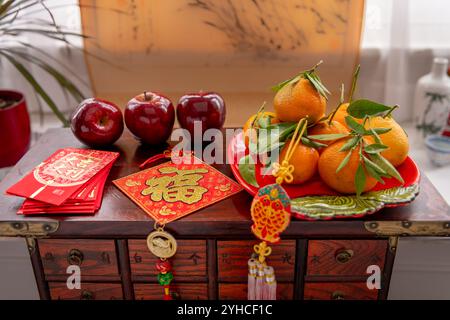 Une assiette de mandarines et de pommes rouges. Paquets rouges et décorations du nouvel an chinois avec des mots de chance, de richesse et de fortune. Un backgr du nouvel an chinois Banque D'Images